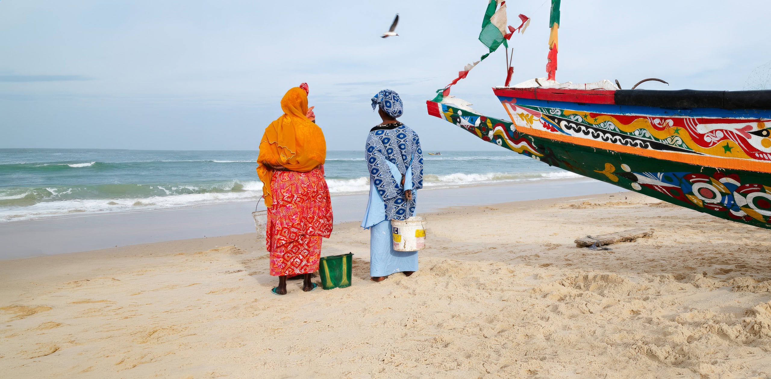 https://www.wildernesstravel.com/wp-content/uploads/2024/02/10-SWAFRICA-two-women-traditional-clothing-fishing-boat-sea-senegal.jpg