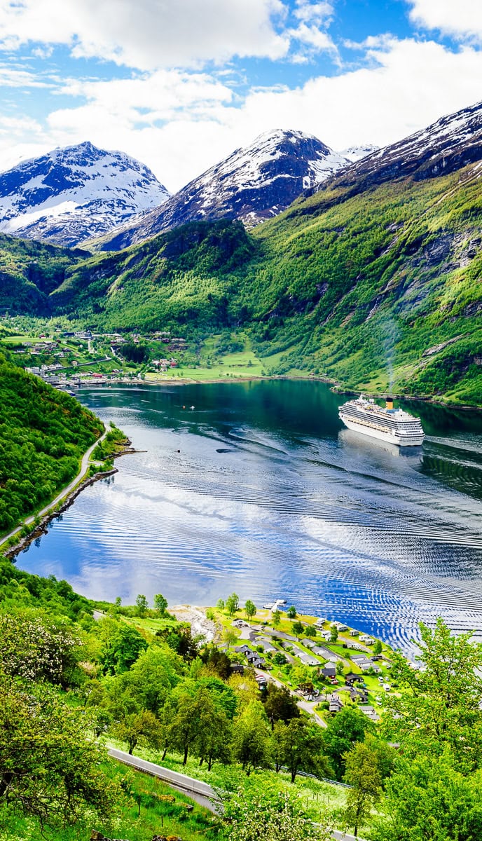 A cruise ship sails through a fjord surrounded by greenery and snow-capped mountains, with a quaint village visible along the shoreline—a scene perfect for SEO blog keywords.