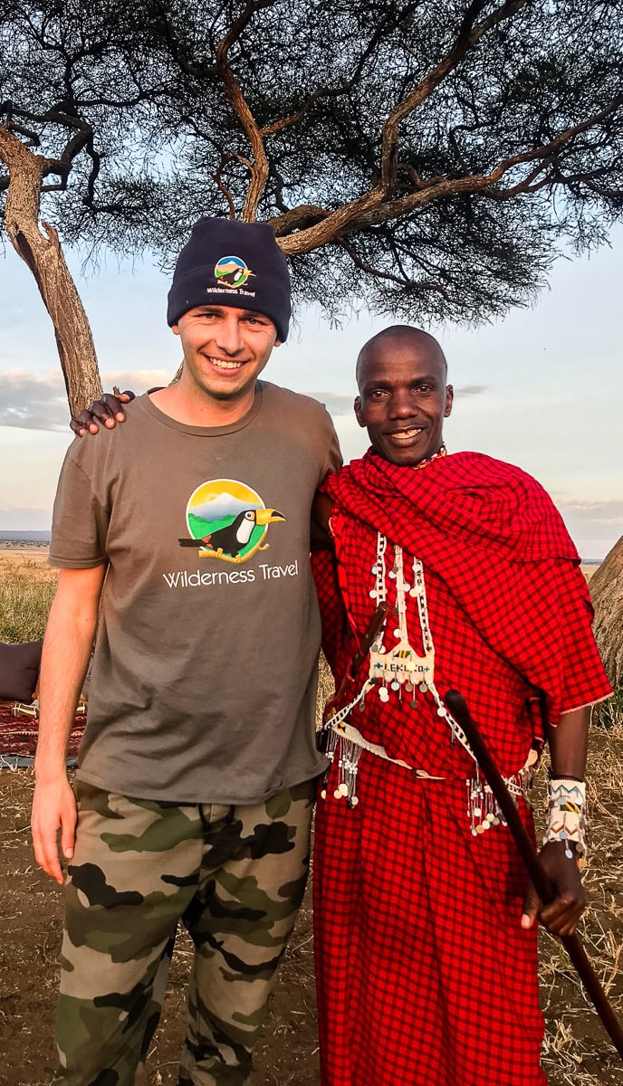 Two people standing together outdoors. The person on the left, dressed in a beanie, T-shirt, and camouflage pants, contrasts with the individual on the right, who is wearing traditional attire and holding a staff. This unique scene could be a captivating image for your blog, boosting SEO effortlessly.