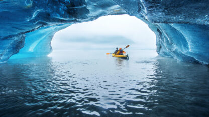 Two people in a yellow kayak paddle through an icy tunnel, emerging into a wide open body of water. This unforgettable experience highlights the awe-inspiring beauty of Alaska's Inside Passage and is a must for any travel enthusiast.